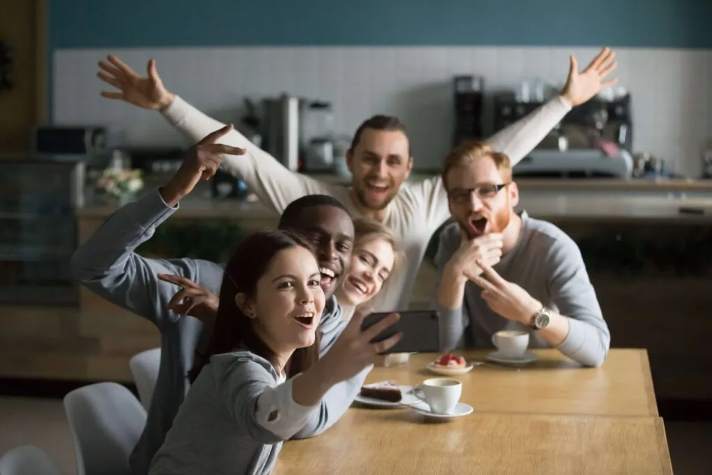 funny-millennial-friends-taking-group-selfie-smartphone-cafe